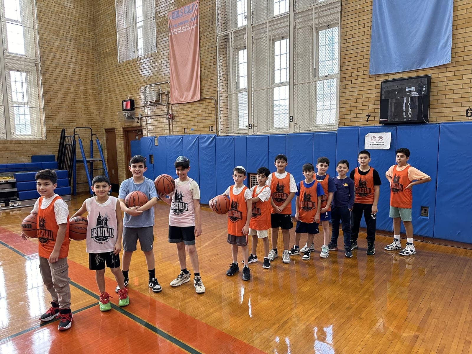 A line of players in BBL NYC pinnies standing across the gym floor, several holding basketballs