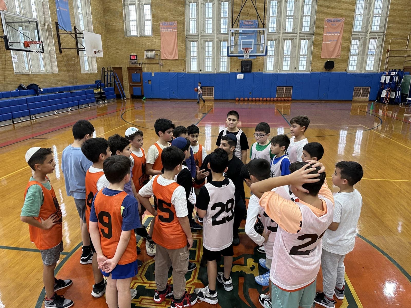 Players in numbered pinnies packed into a huddle at center court
