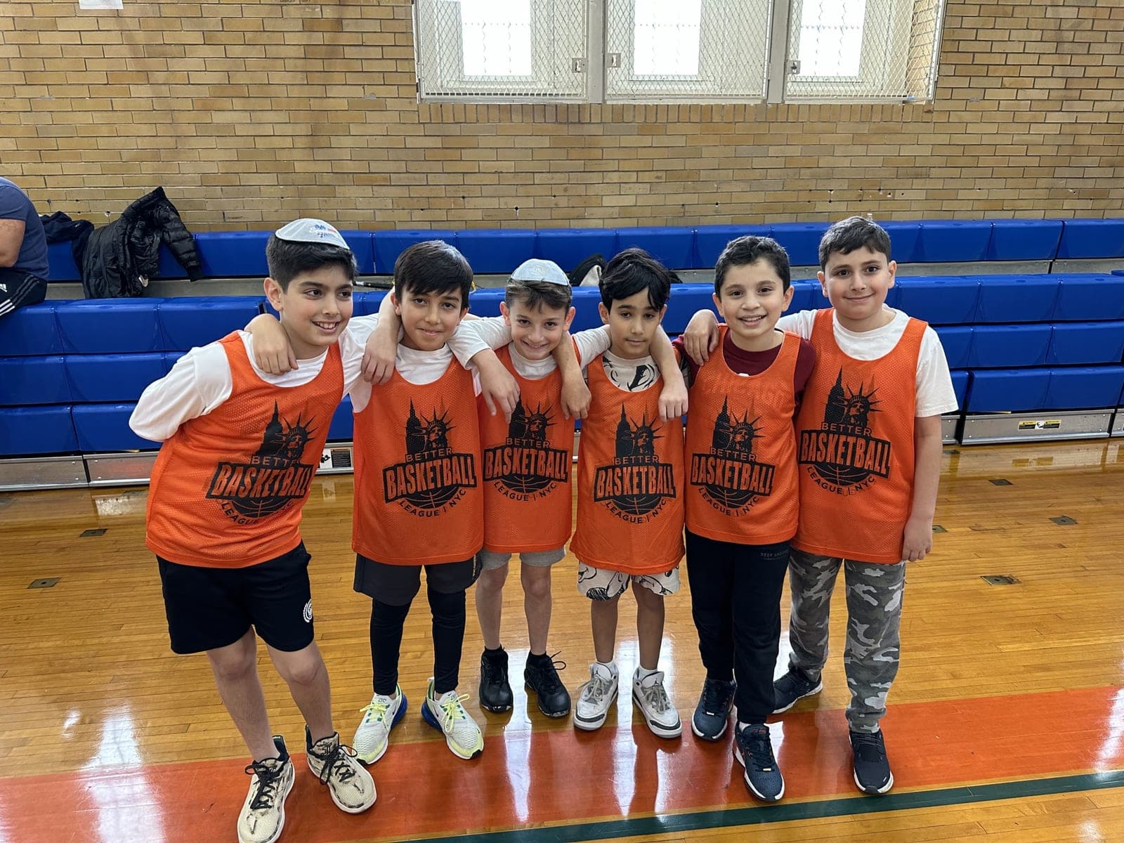 A group in orange pinnies standing arm in arm in front of the bleachers